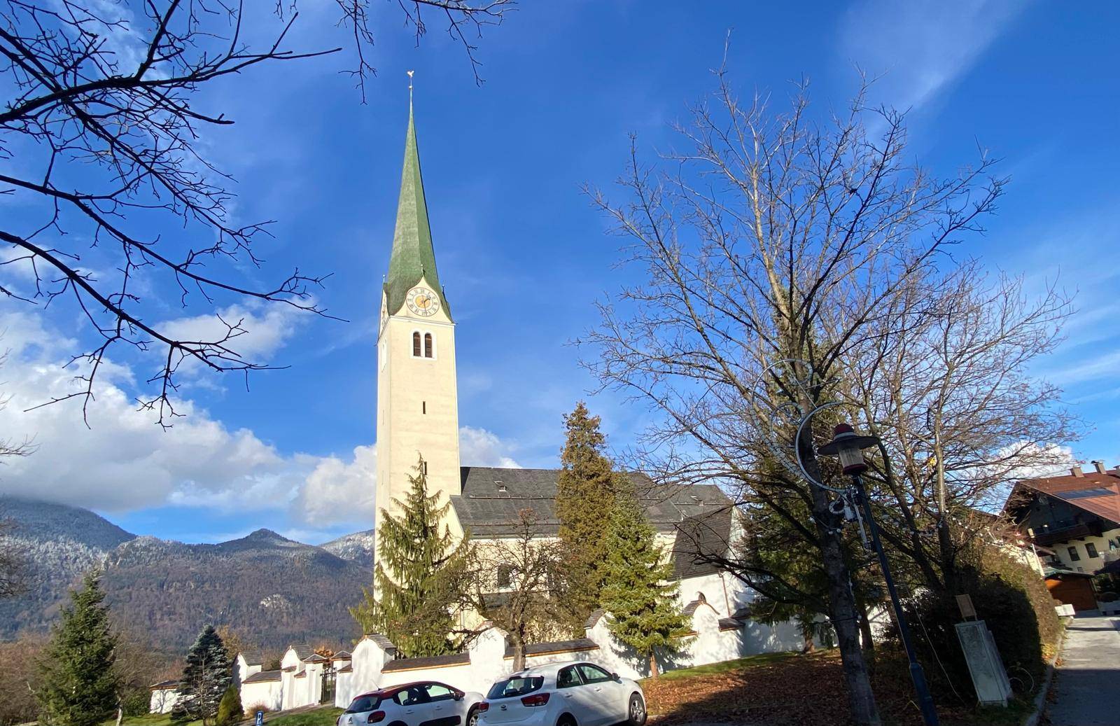 Malerische Kirche mit hohem Turm vor einer Kulisse aus schneebedeckten Bergen und blauem Himmel.