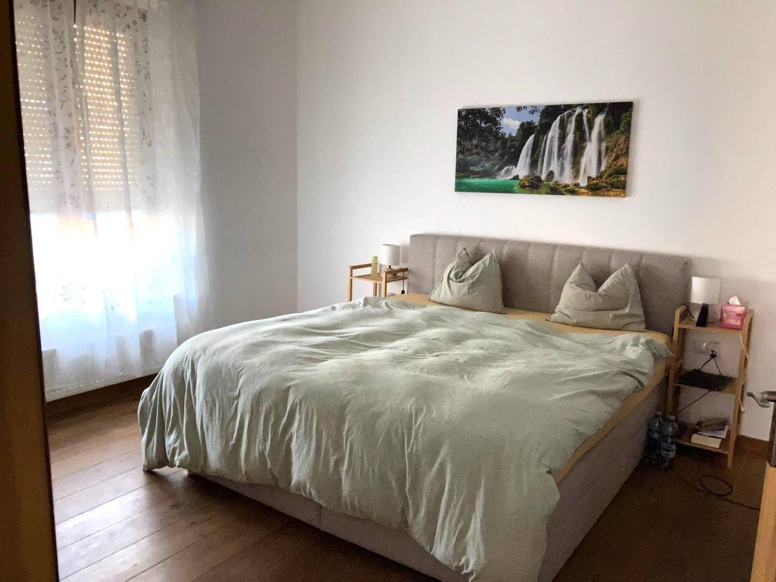 Gemütliches Schlafzimmer mit großem Bett, Holzboden und einem Fenster mit Vorhängen.
