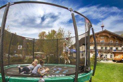 Kinder spielen auf einem großen Trampolin im Garten mit dem Gasthaus im Hintergrund.