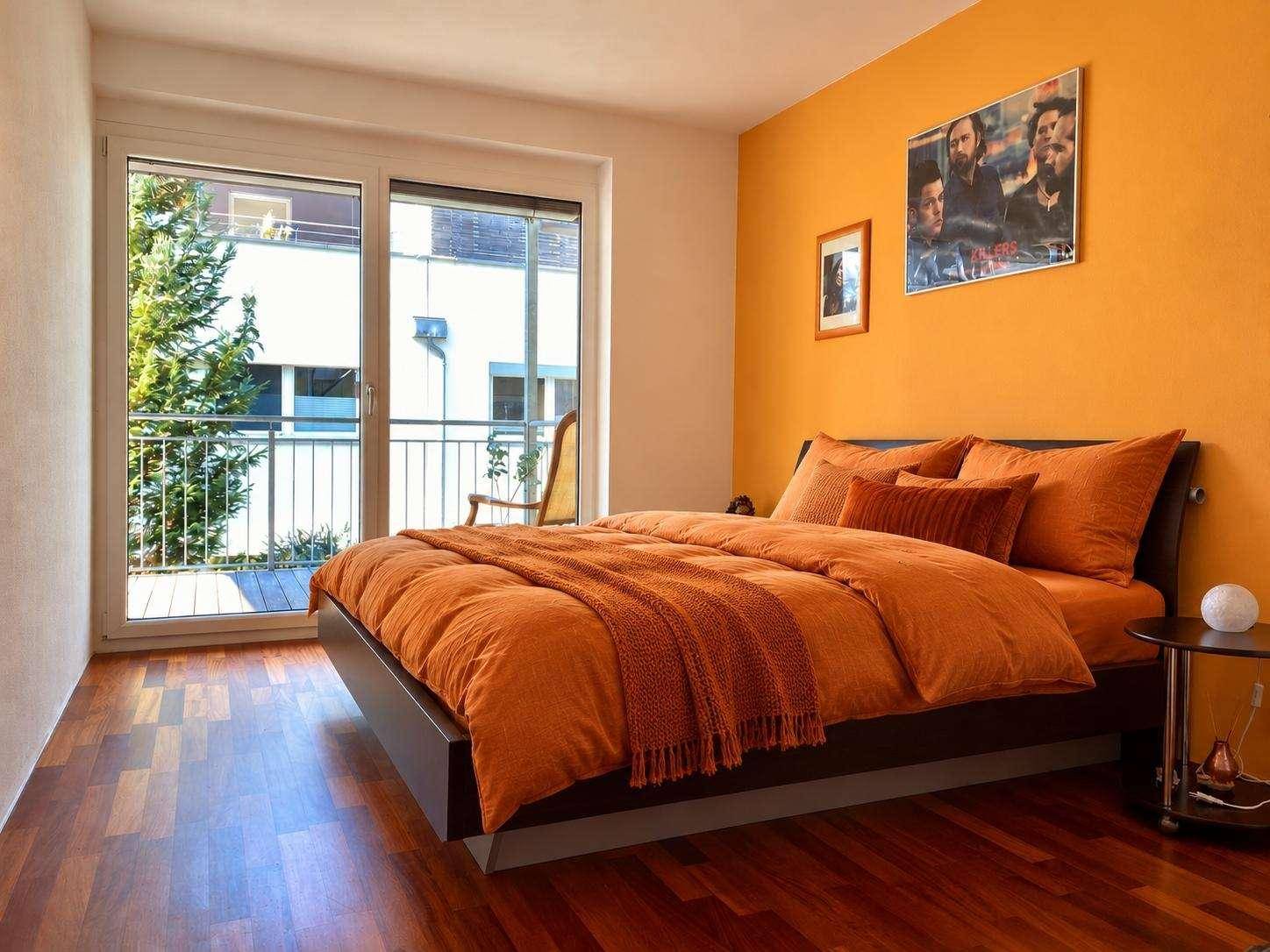 Schlafzimmer mit Holzboden, orangefarbenen Wänden und Zugang zu einem Balkon mit Ausblick.