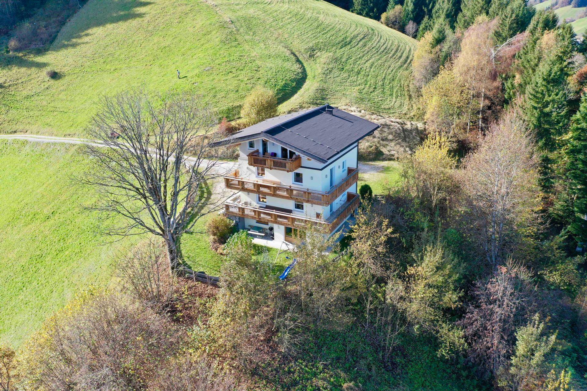 Luftaufnahme des Hauses in einer weitläufigen grünen Hügellandschaft mit Bergen im Hintergrund.
