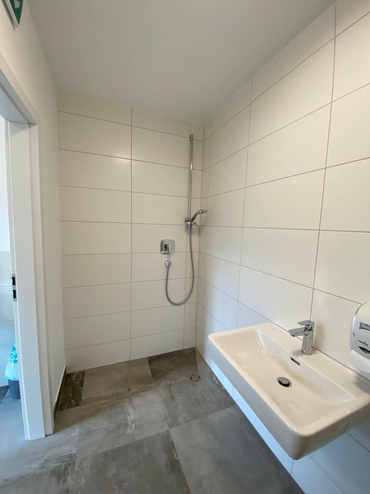 Modernes Badezimmer mit weiß gefliesten Wänden, grauen Bodenfliesen und einer Dusche, sauber und funktional.