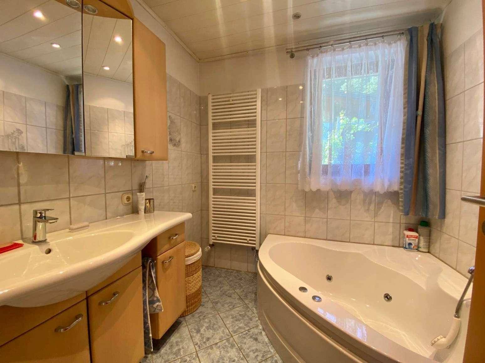 Gefliestes Badezimmer mit Eckbadewanne, Einzelwaschbecken und beheiztem Handtuchhalter.