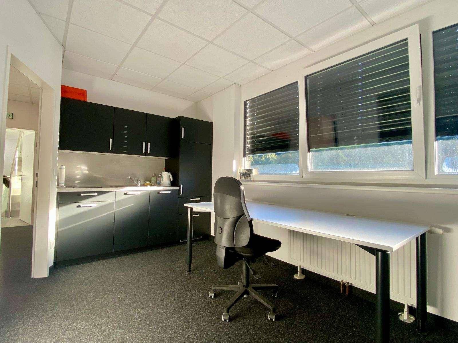 Büroraum mit integrierter Küchenzeile, Schreibtisch und Bürostuhl, bietet eine praktische Arbeitsumgebung.