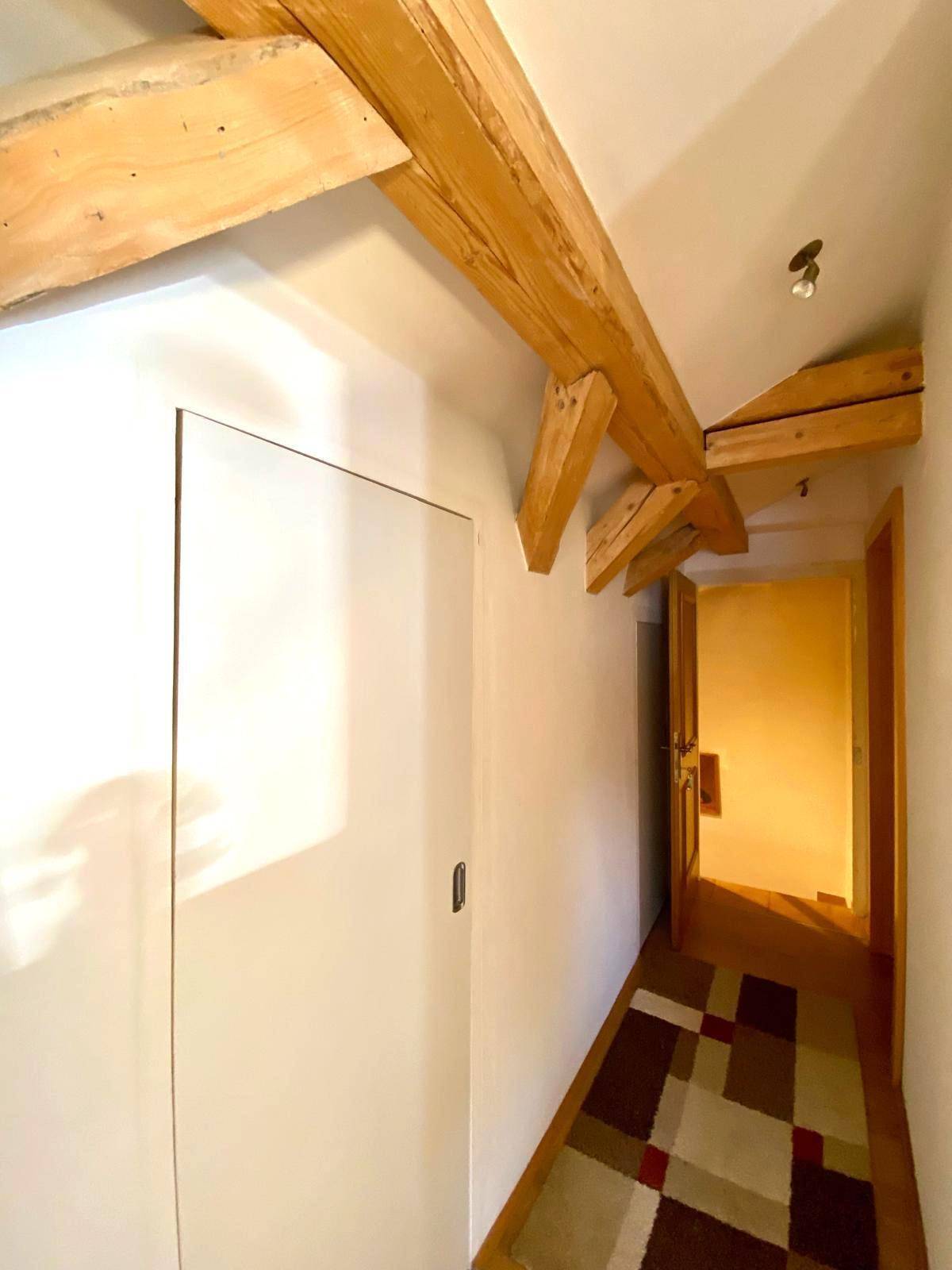 Heller Flur im Dachgeschoss mit sichtbaren Holzbalken und Teppichläufer.
