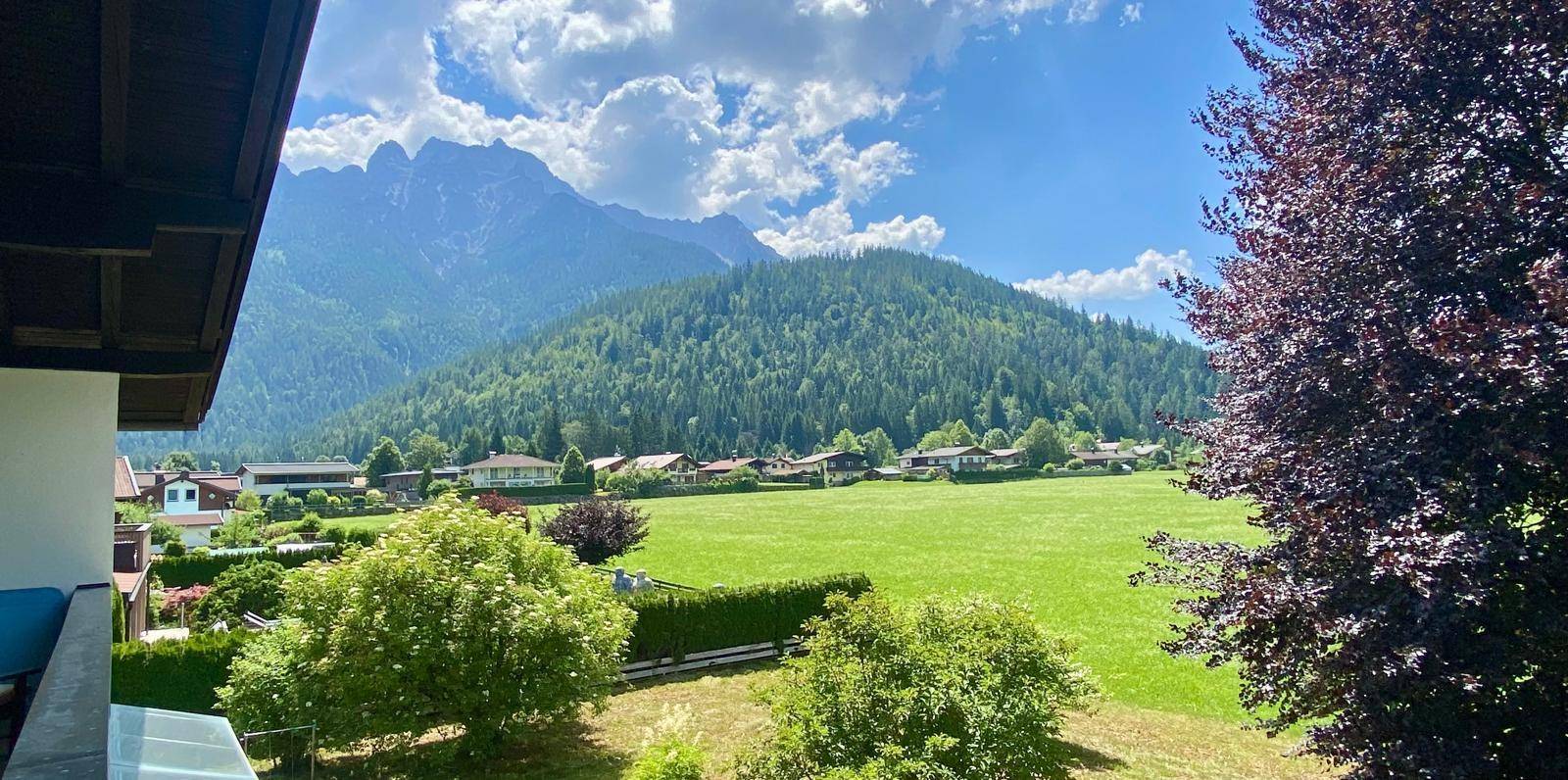 Panoramablick vom Balkon auf weite grüne Felder, ein Dorf und majestätische Berge.