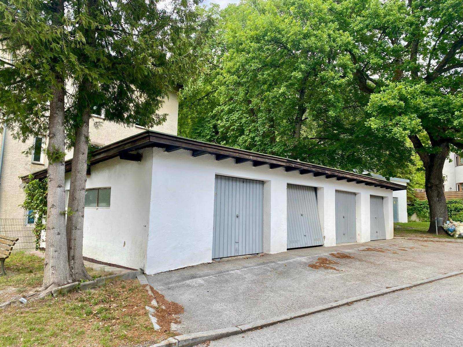 Lange Reihe von Garagenboxen mit grauen Toren und weißer Fassade, umgeben von Bäumen.
