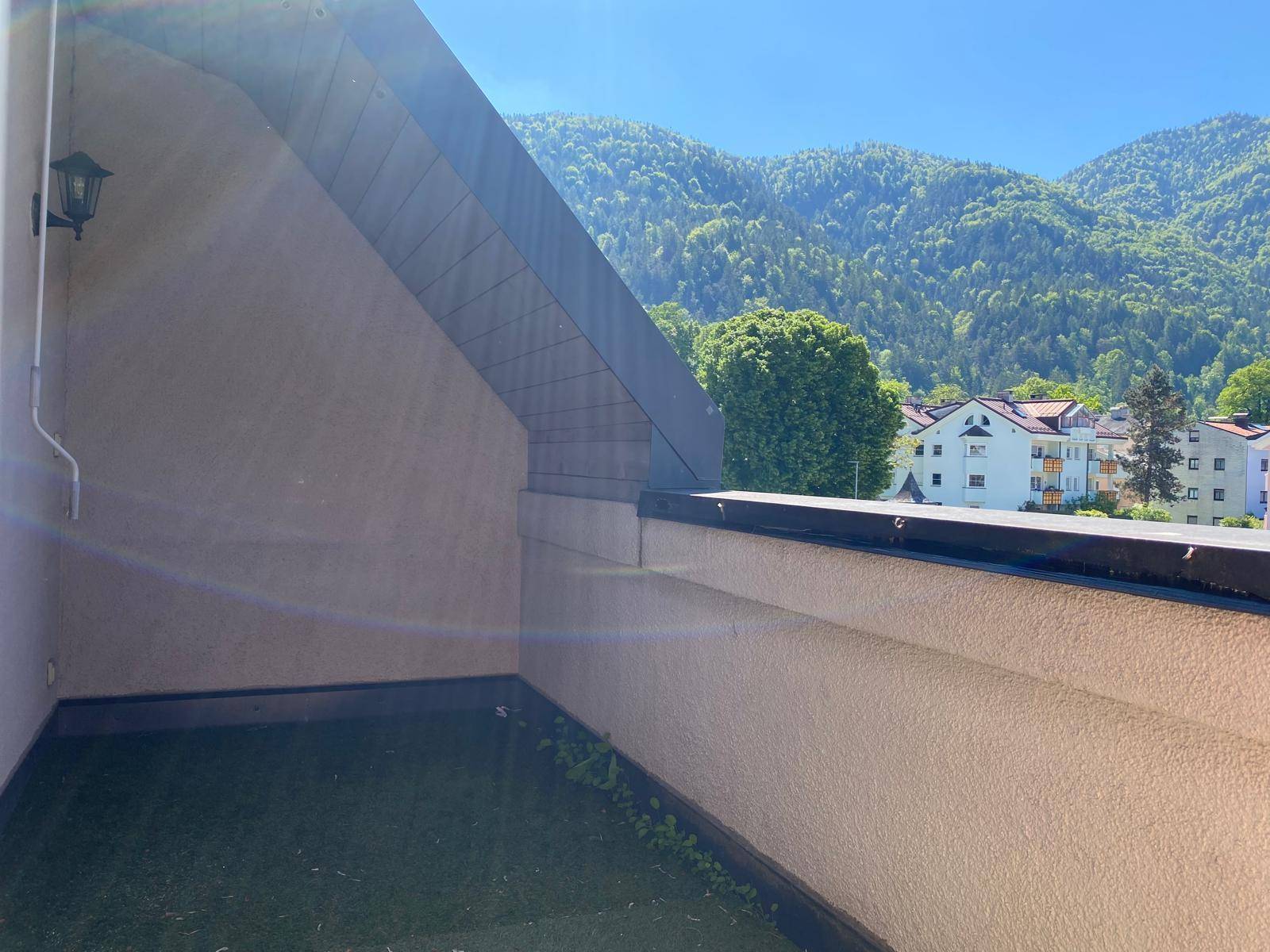 Kleiner Balkon mit Blick auf die umliegenden Berge und die darunter liegende Wohnbebauung.