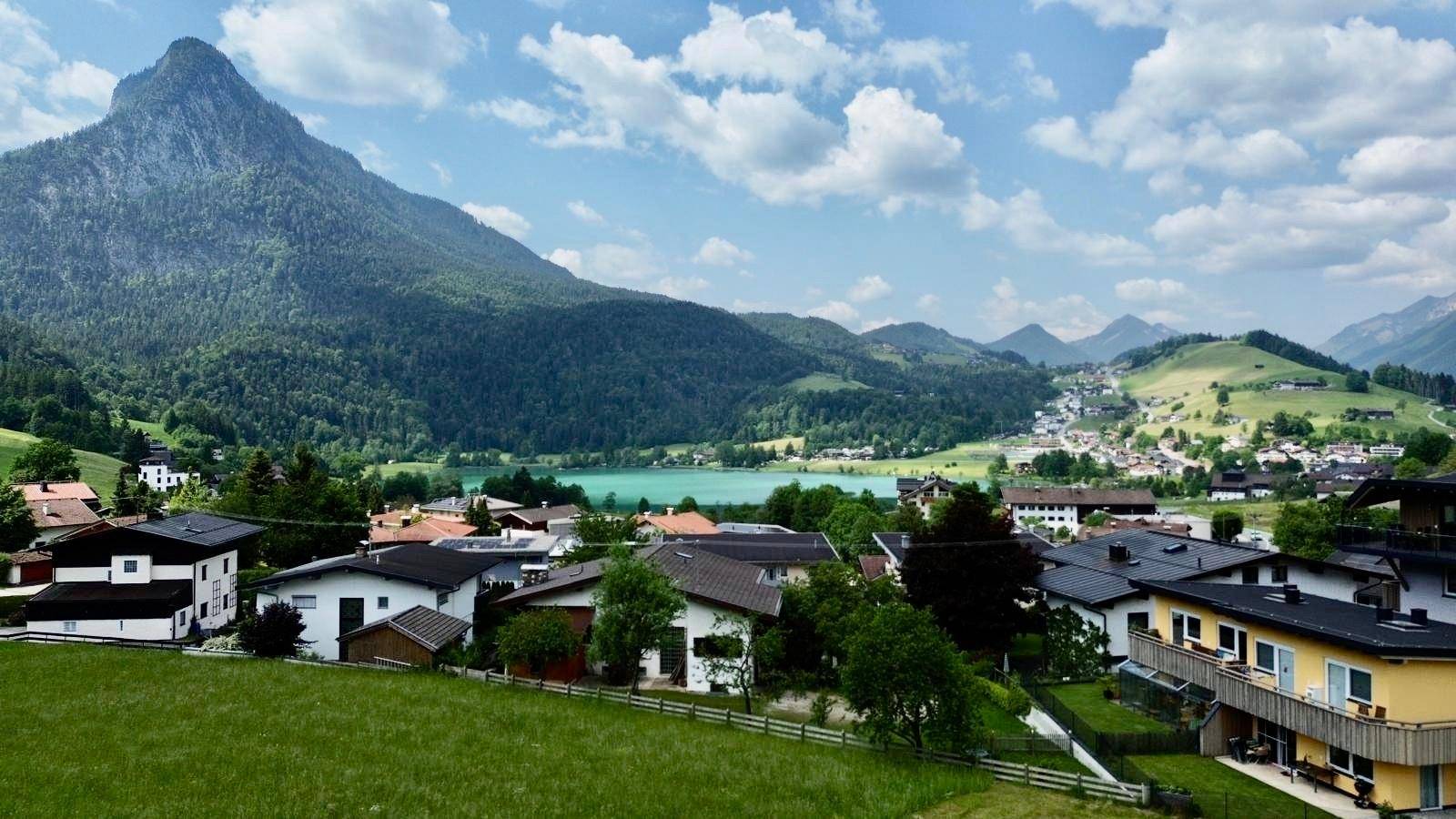 Malerische Landschaftsaufnahme mit See, Bergen und Häusern in einer ländlichen Umgebung.