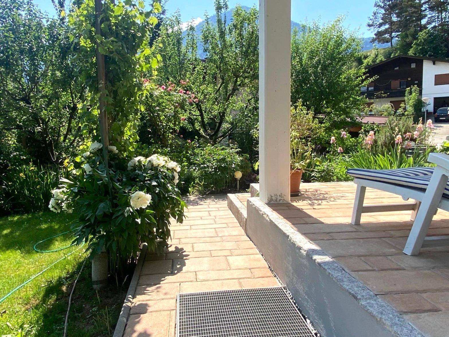 Gepflasterter Terrassenbereich mit Sitzgelegenheit und Blick ins Grüne, umgeben von Pflanzen.