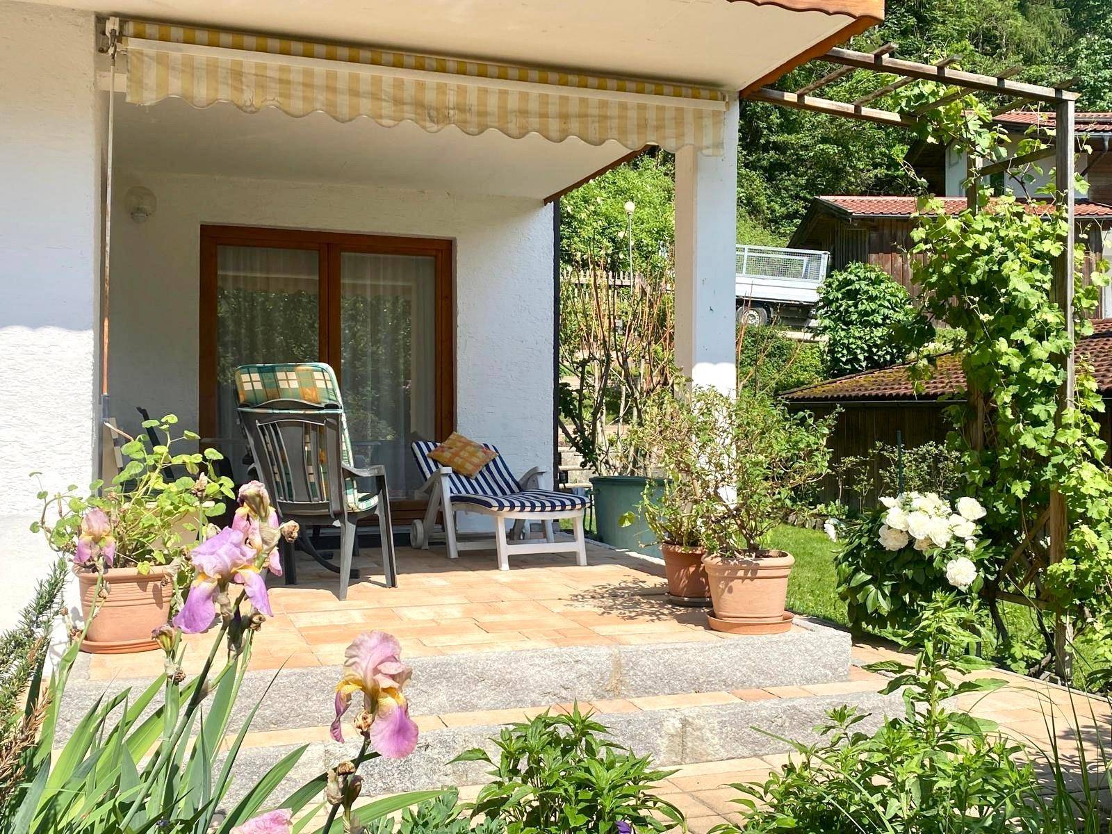 Gemütliche Terrasse mit Markise und Gartenmöbeln, umgeben von blühenden Pflanzen und viel Grün.