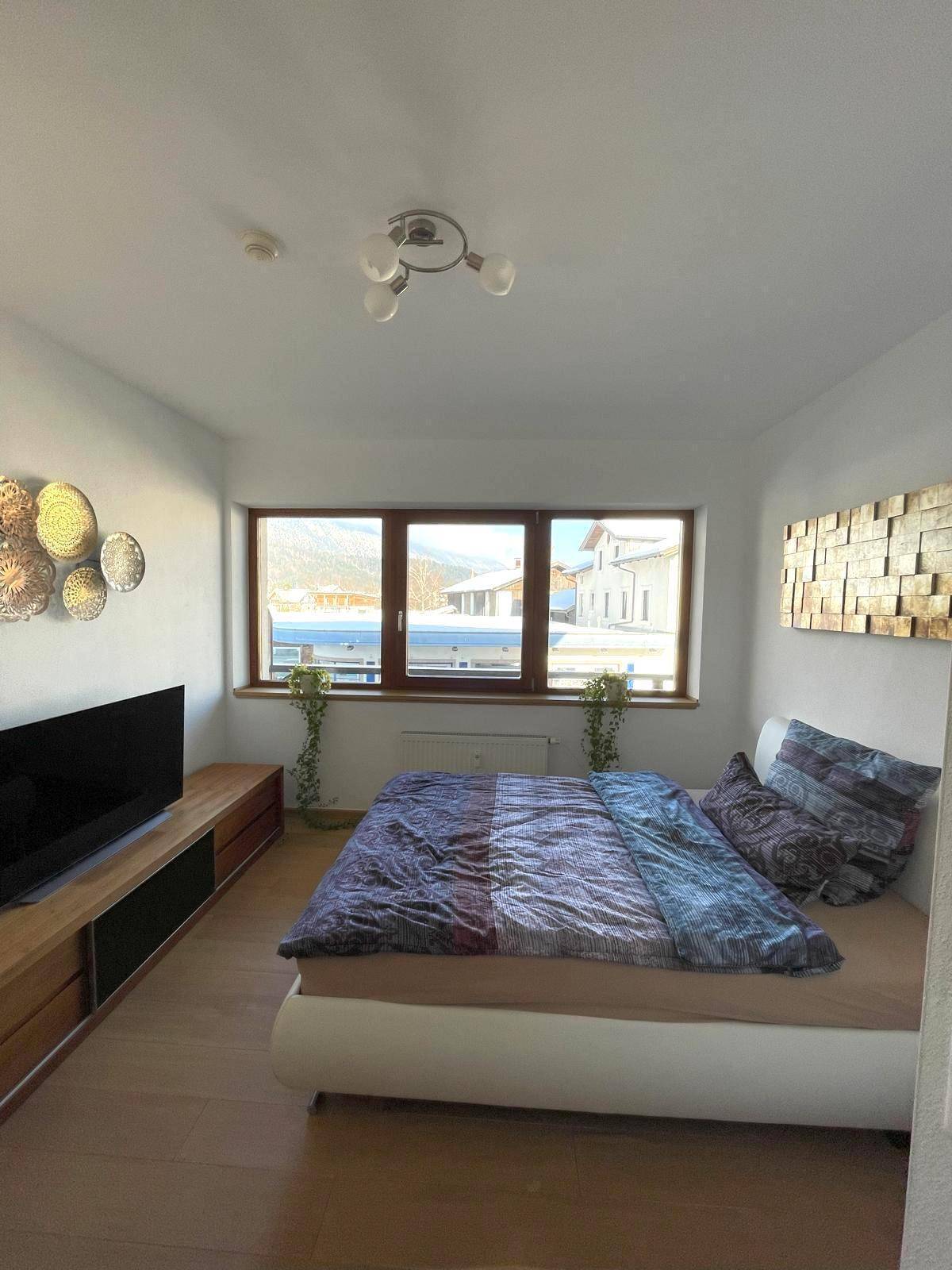 Modern eingerichtetes Schlafzimmer mit Doppelbett, Holzboden und großen Fenstern.