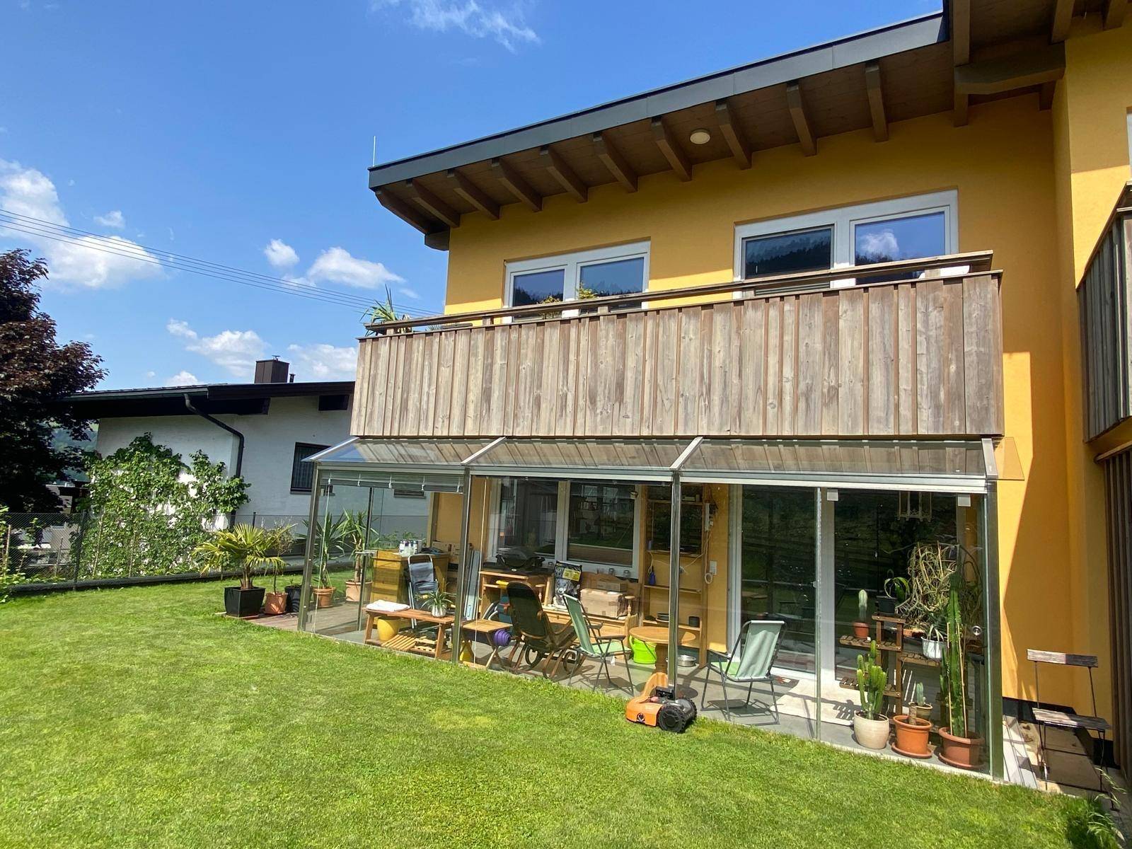 Rückansicht des Hauses mit Wintergarten, Balkon und gepflegtem Rasenbereich.