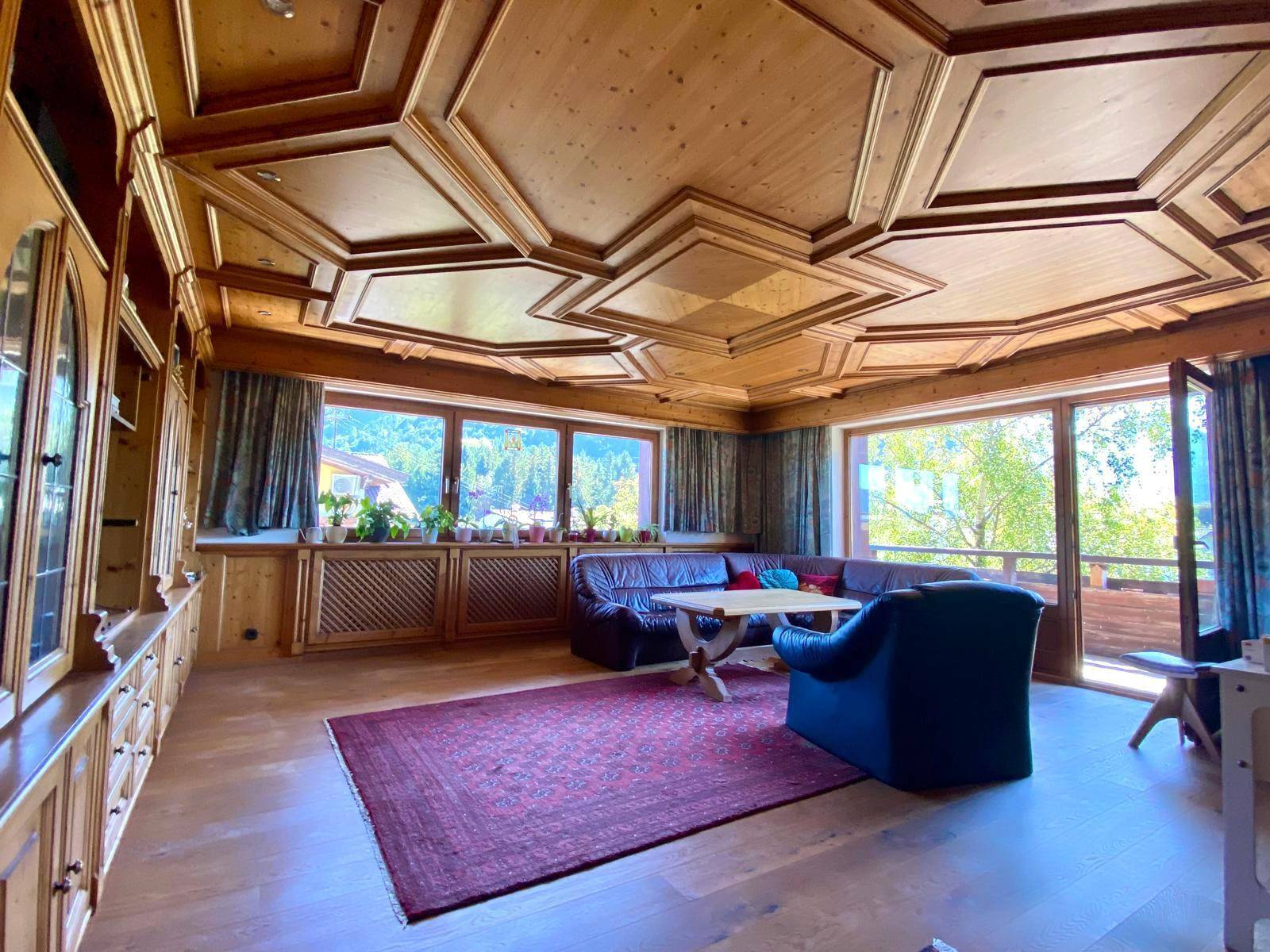 Geräumiges Wohnzimmer mit Holztäfelung, Kassettendecke und großen Fenstern mit Bergblick.