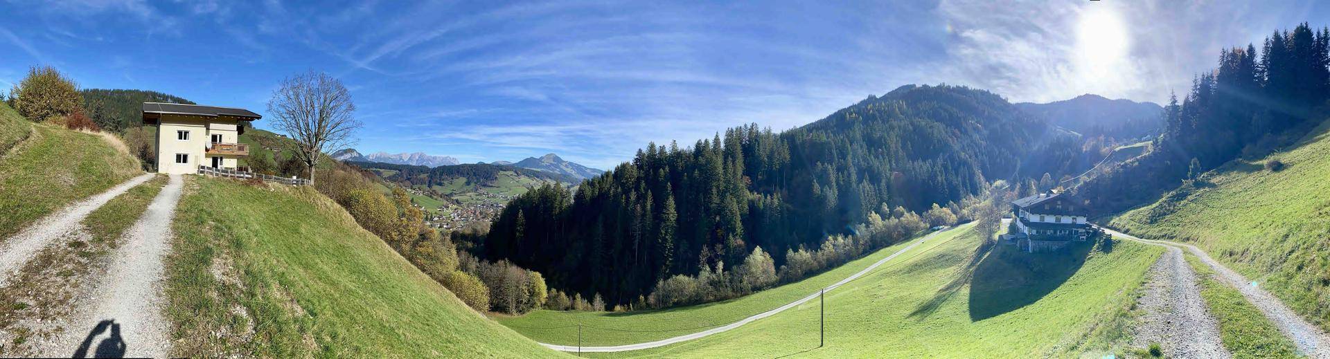 Weitläufige Panoramaansicht der hügeligen Landschaft mit dem Haus im Hintergrund und Bergen.