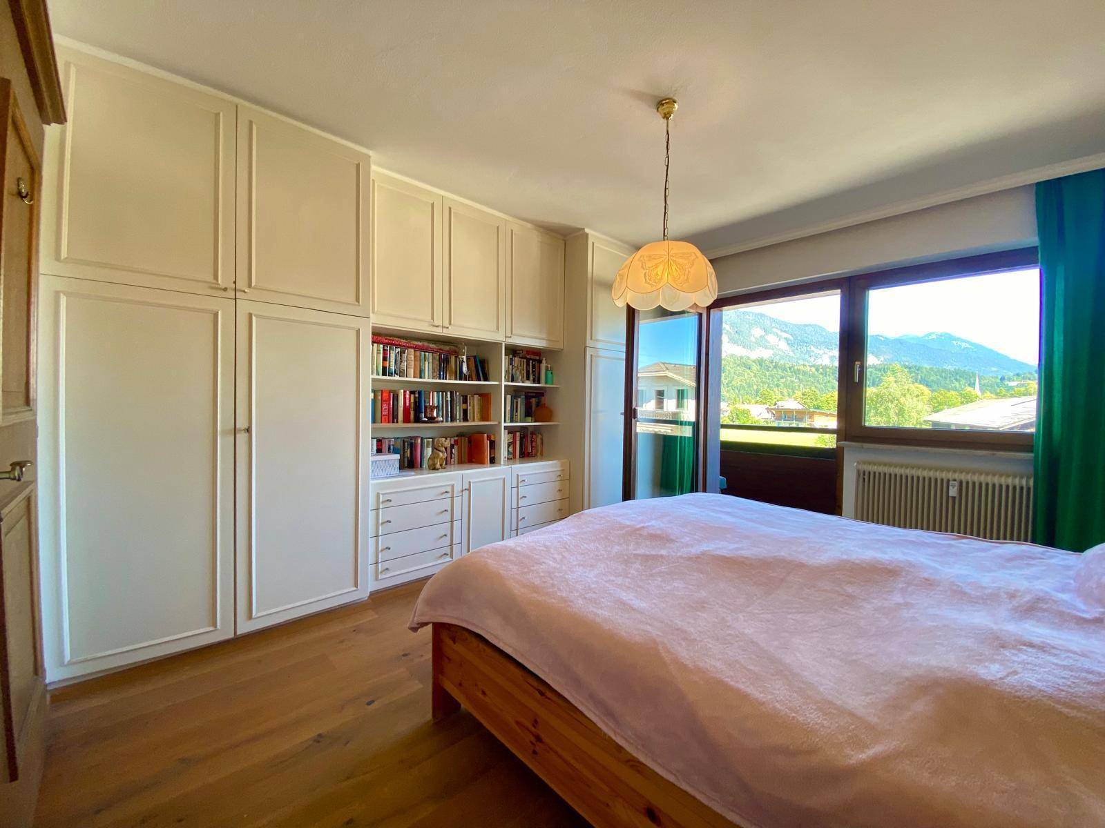 Helles Schlafzimmer mit Einbauschränken, Holzboden und Zugang zu einem Balkon mit Bergblick.