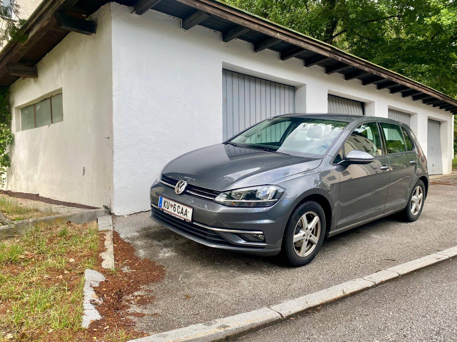Vorderansicht des grauen VW Golfs vor dem Garagengebäude mit weißer Fassade und Garagentoren.