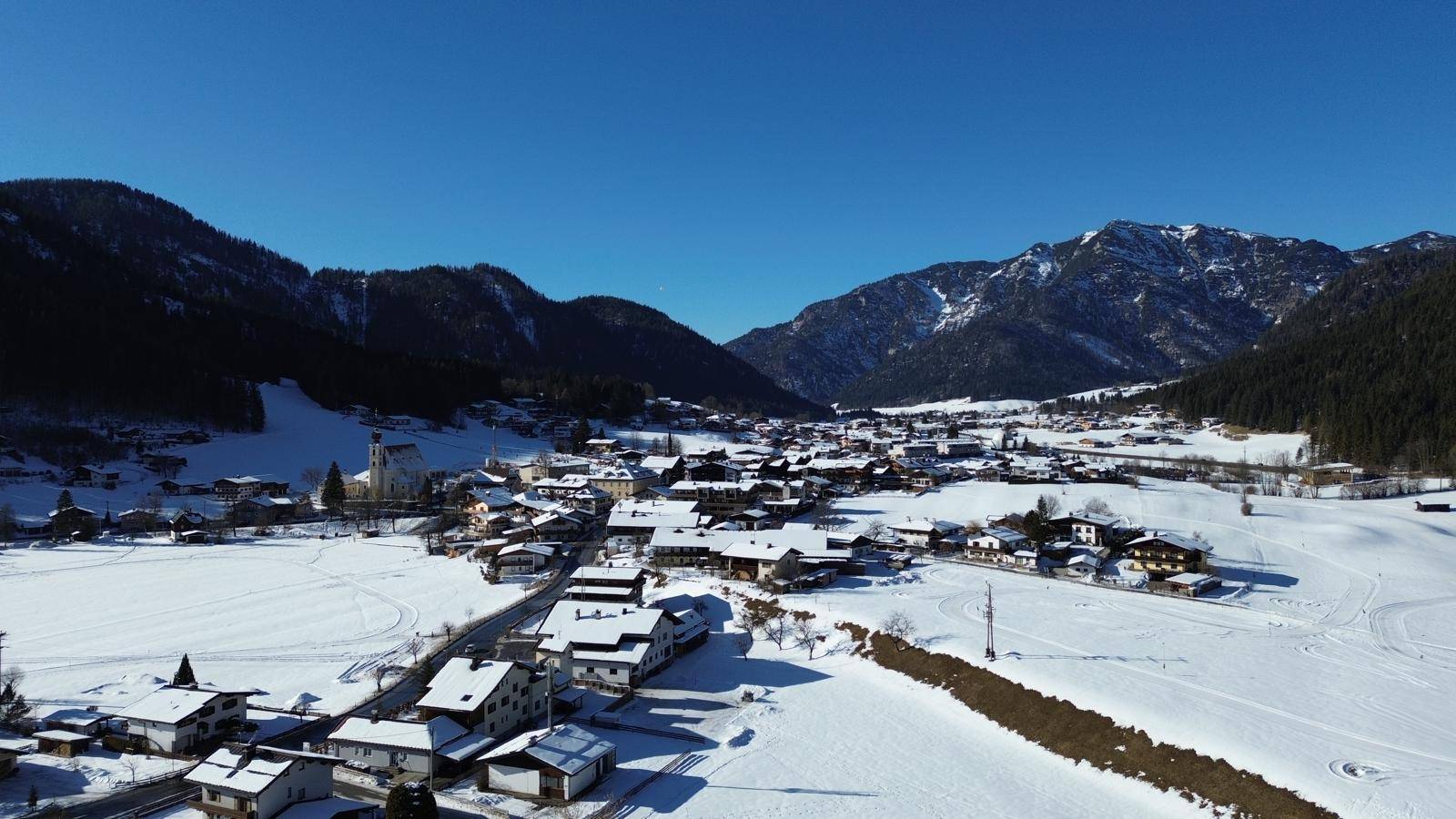 Weitläufige Luftaufnahme einer verschneiten Berglandschaft mit Dorf.