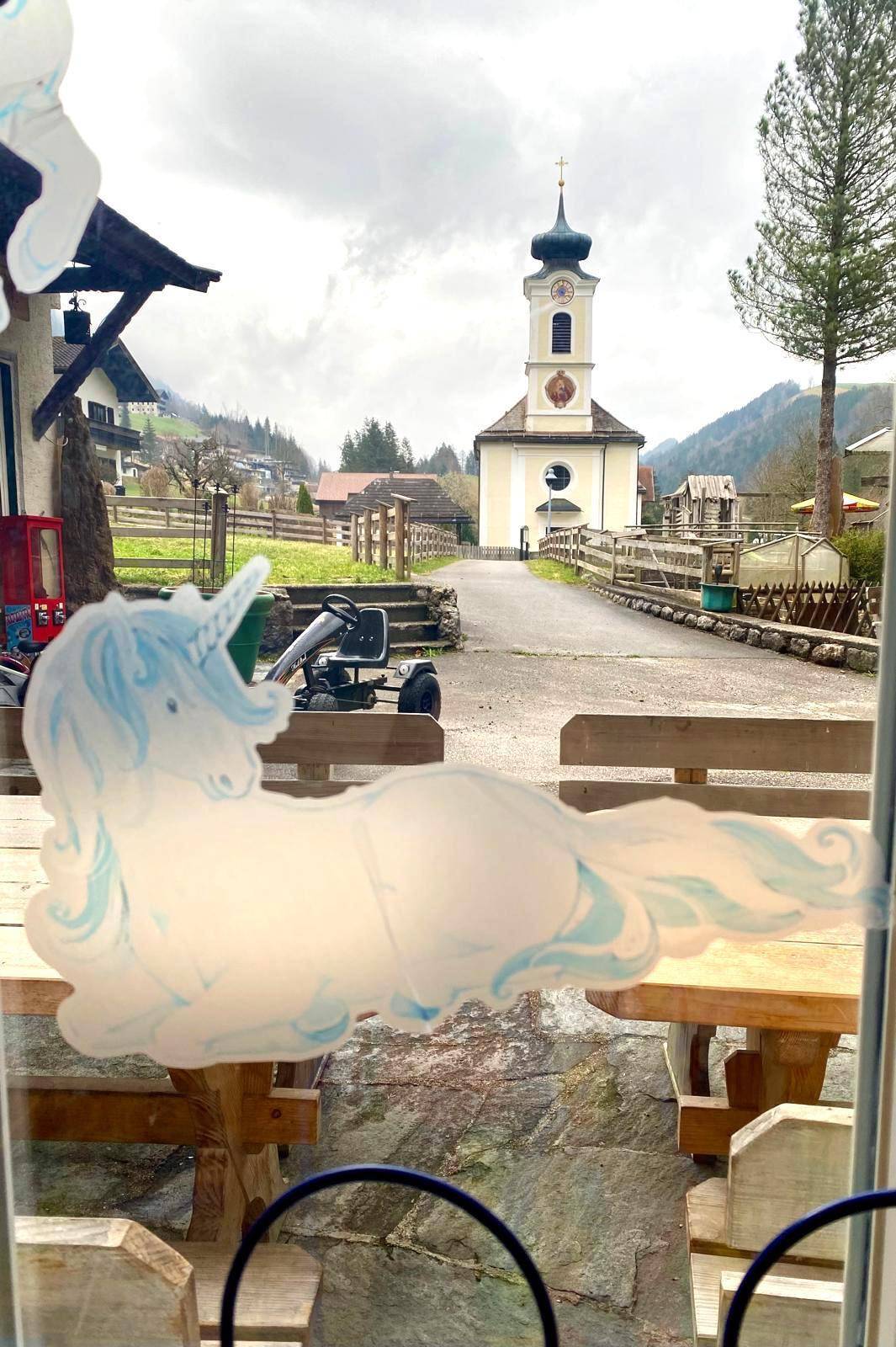 Blick aus dem Fenster auf eine Dorfkirche und die umliegende Landschaft an einem bewölkten Tag.