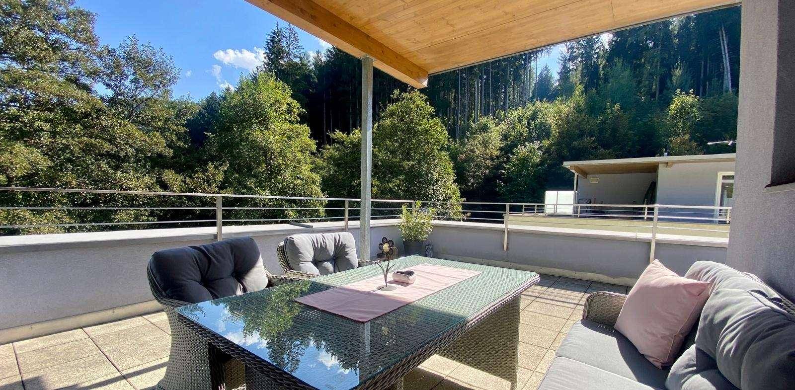 Große Sonnenterrasse mit modernen Gartenmöbeln und weitem Blick auf den Wald.