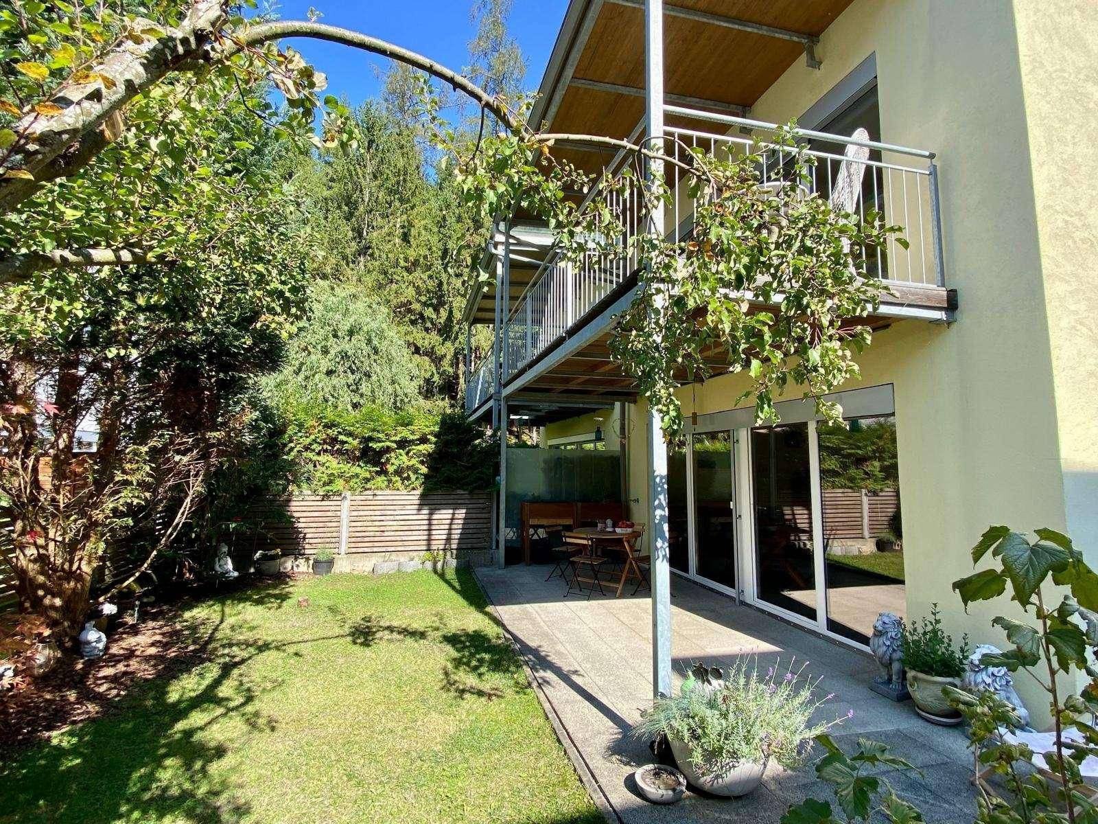 Seitlicher Blick auf das Gebäude mit gepflegtem Garten, Terrasse und darüberliegenden Balkonen.