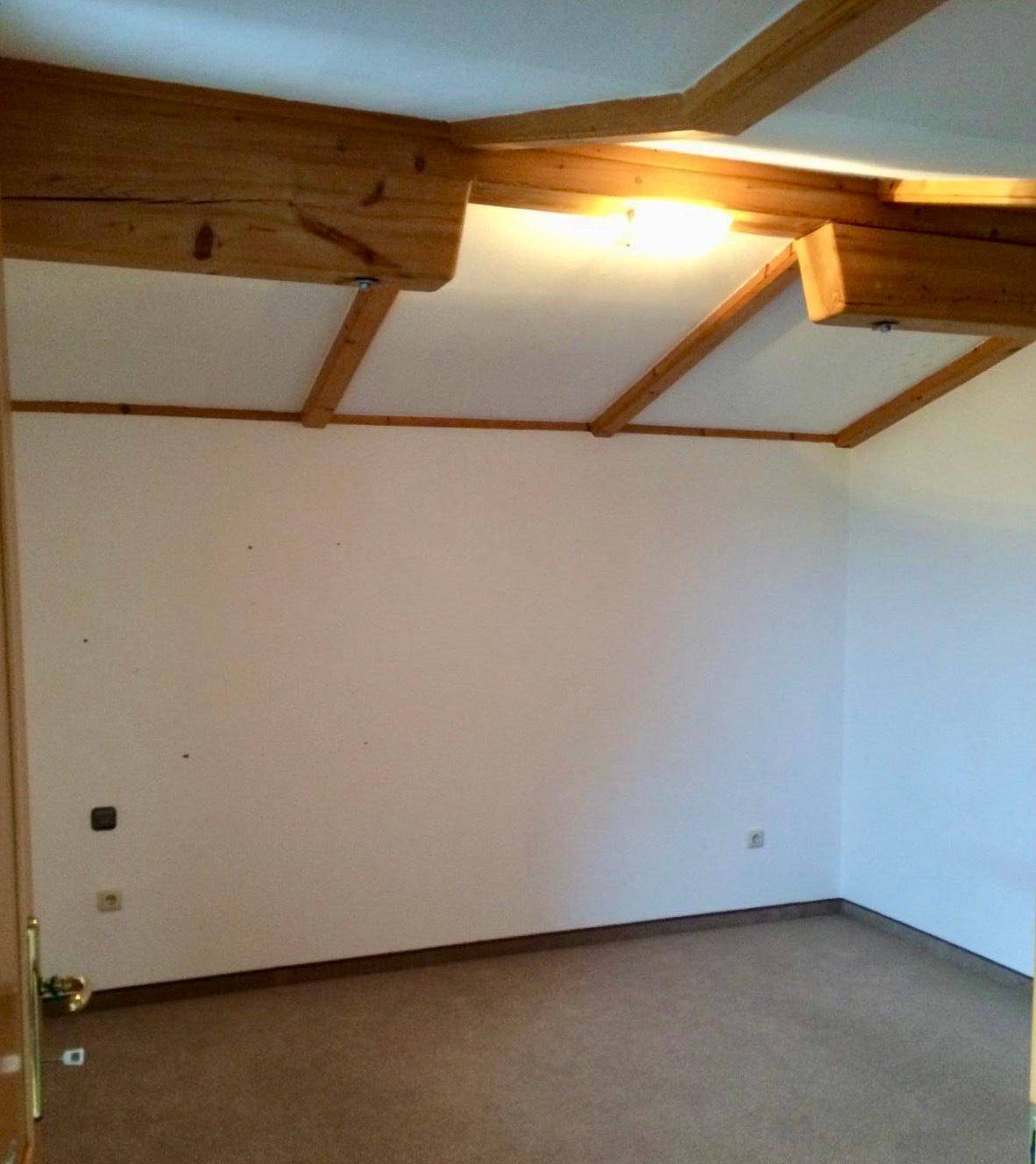 Schlafzimmer mit Holzbalken an der Decke und Teppichboden, bereit zur Einrichtung.