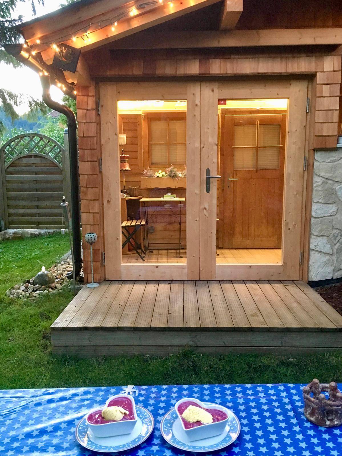 Gemütlicher Außenbereich mit Holzdeck vor einem kleinen Holzhaus, ideal für Mahlzeiten im Freien.