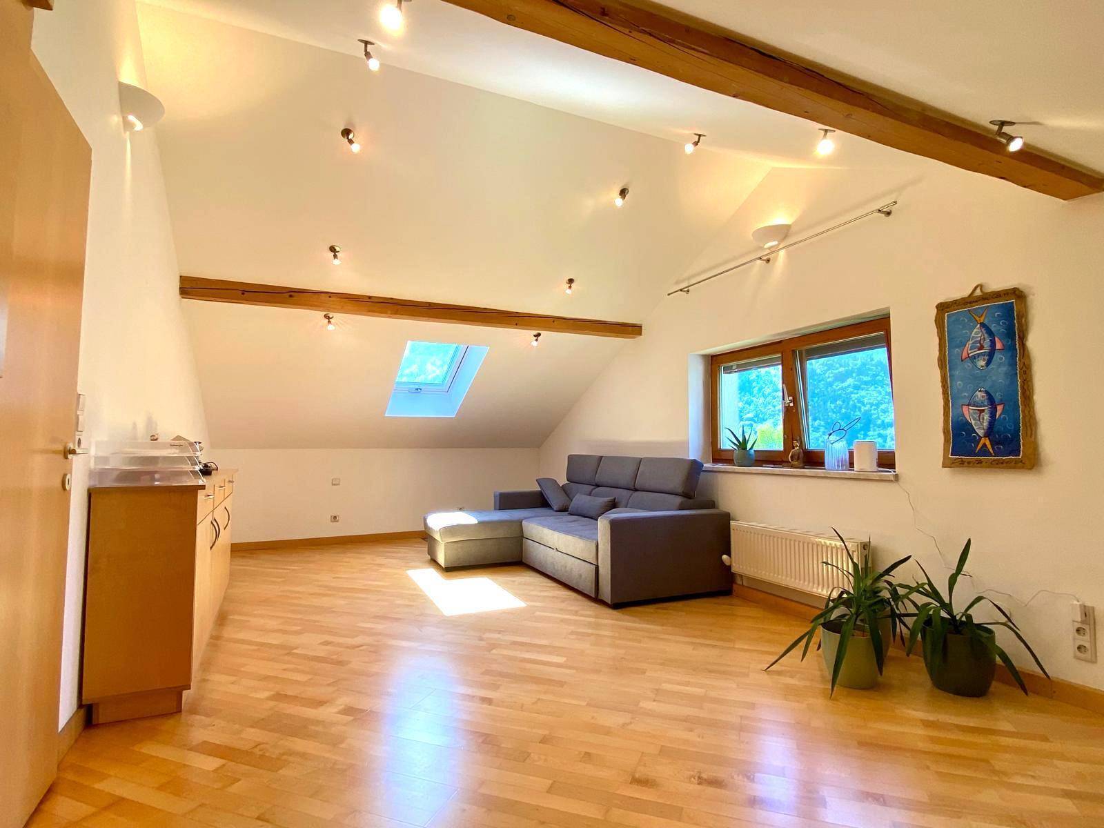 Dachgeschoss-Wohnzimmer mit Holzbalken, Schrägen und Dachfenster, modern eingerichtet.