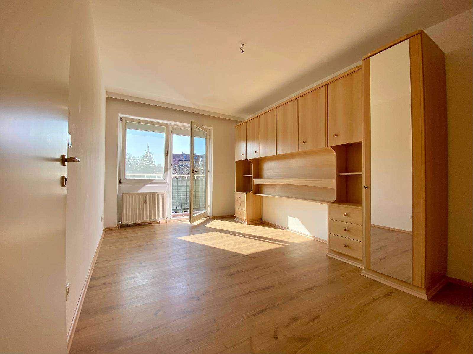 Helles Schlafzimmer mit Einbauschränken, Laminatboden und Zugang zu einem Balkon.
