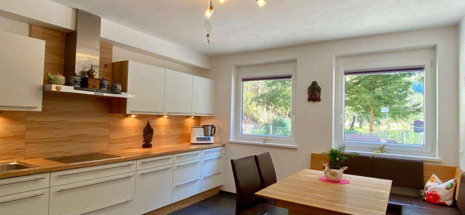 Moderne Einbauküche mit weißen Schränken, Holzarbeitsplatten und Essbereich am Fenster mit Ausblick.
