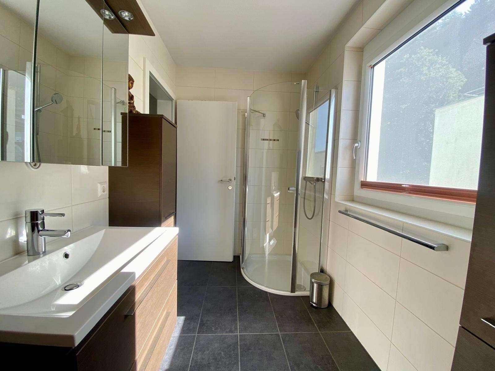 Helles Badezimmer mit Duschkabine, modernem Waschtisch und Fenster für natürliches Tageslicht.