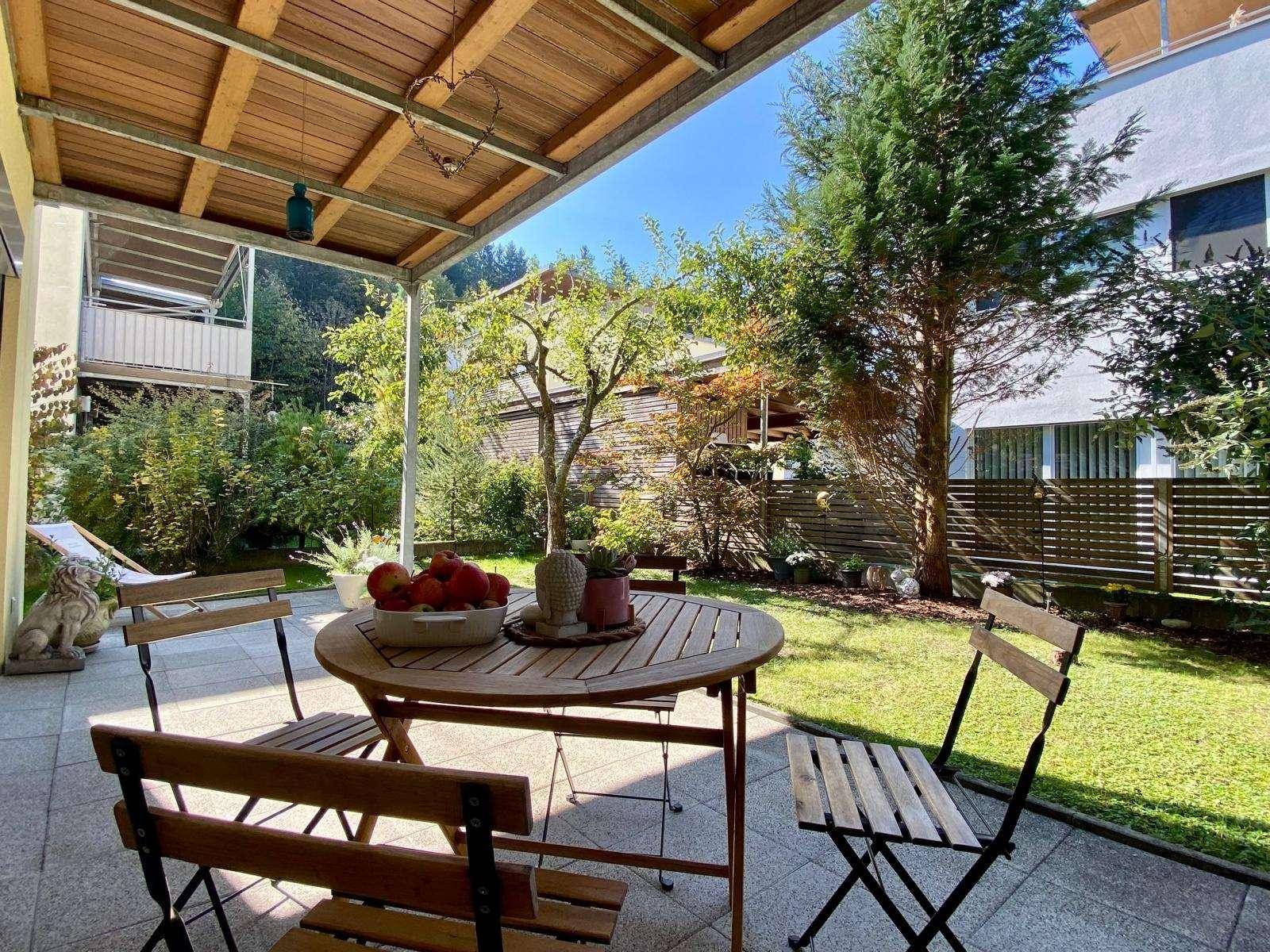 Überdachte Terrasse mit Holztisch und Gartenblick, ideal für entspannte Stunden im Freien.