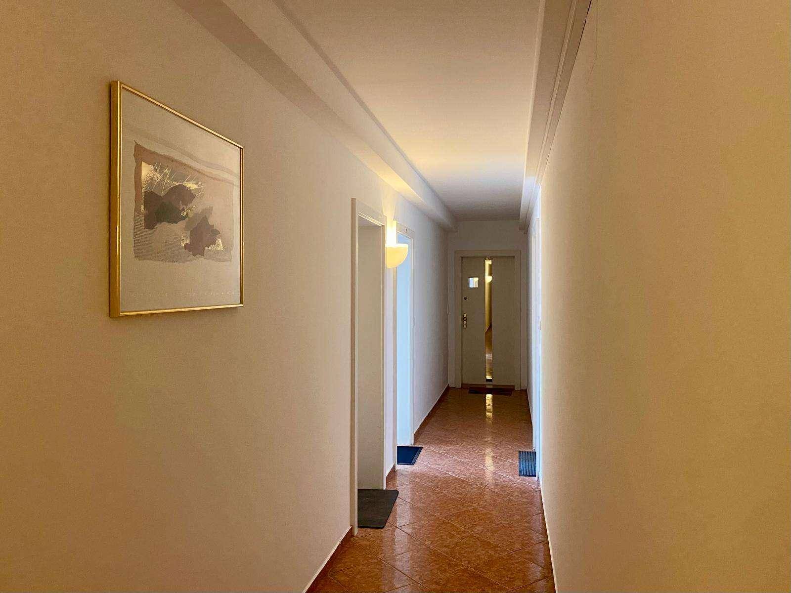 Langer Flur mit Terrakotta-Fliesenboden und einem Gemälde an der Wand.
