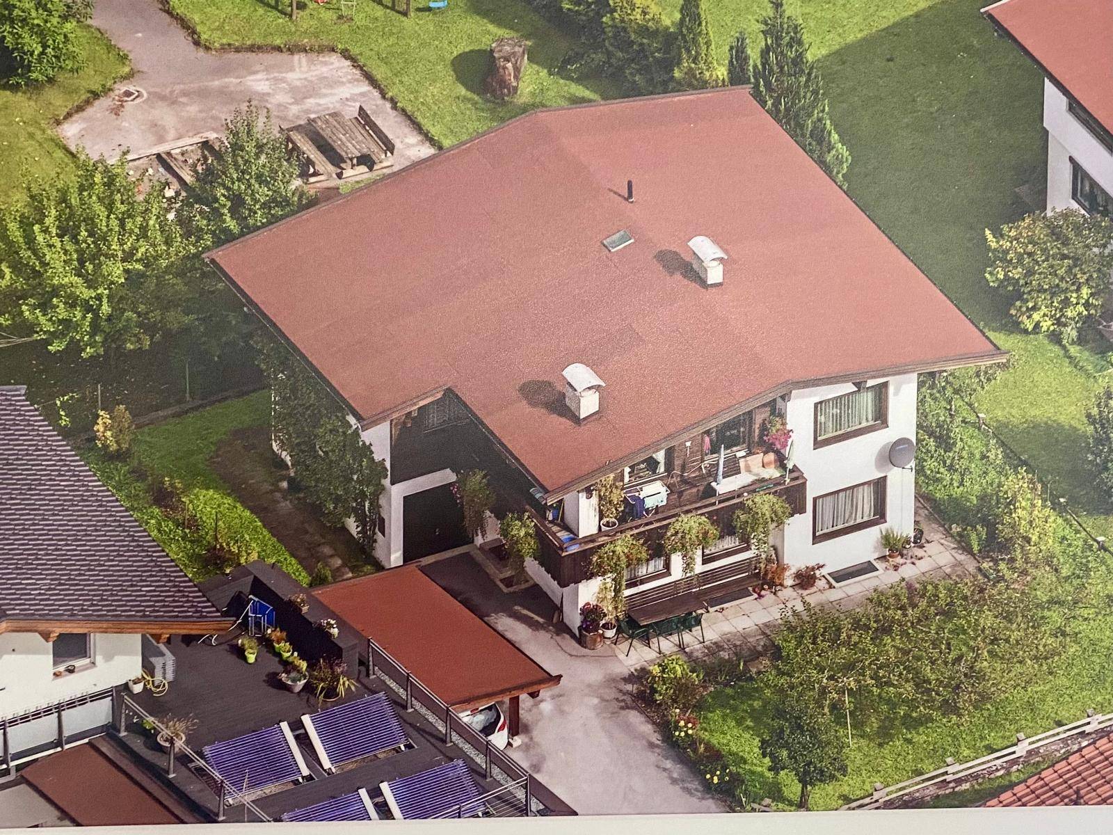 Luftaufnahme eines Hauses mit rotem Satteldach, Garten und umliegender Grünfläche.