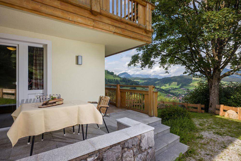 Gemütliche Terrasse mit Esstisch und Stühlen, umgeben von grüner Natur und Bergblick.