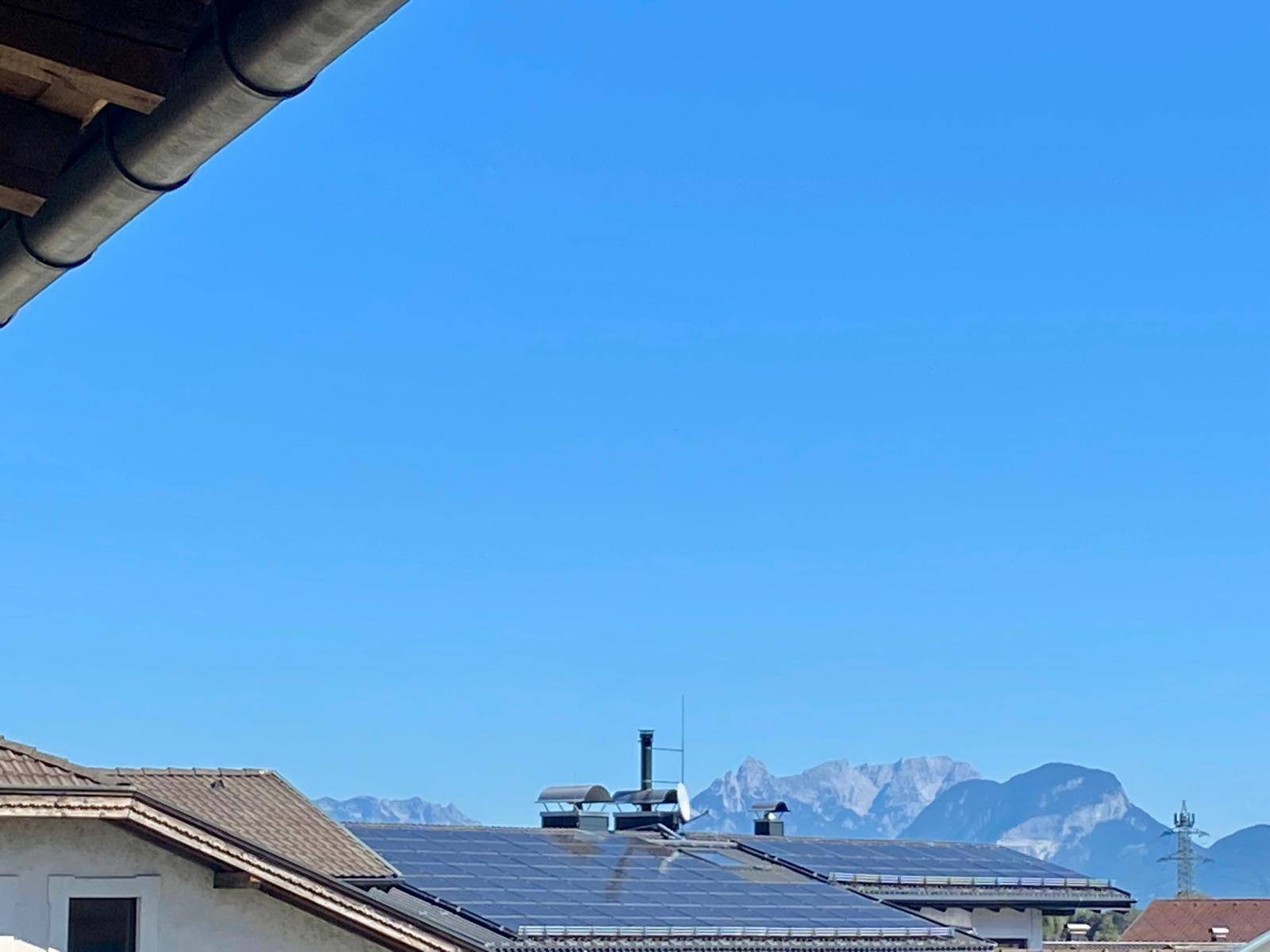 Blick über Dächer mit Solaranlagen auf die majestätische Bergkette im Hintergrund.
