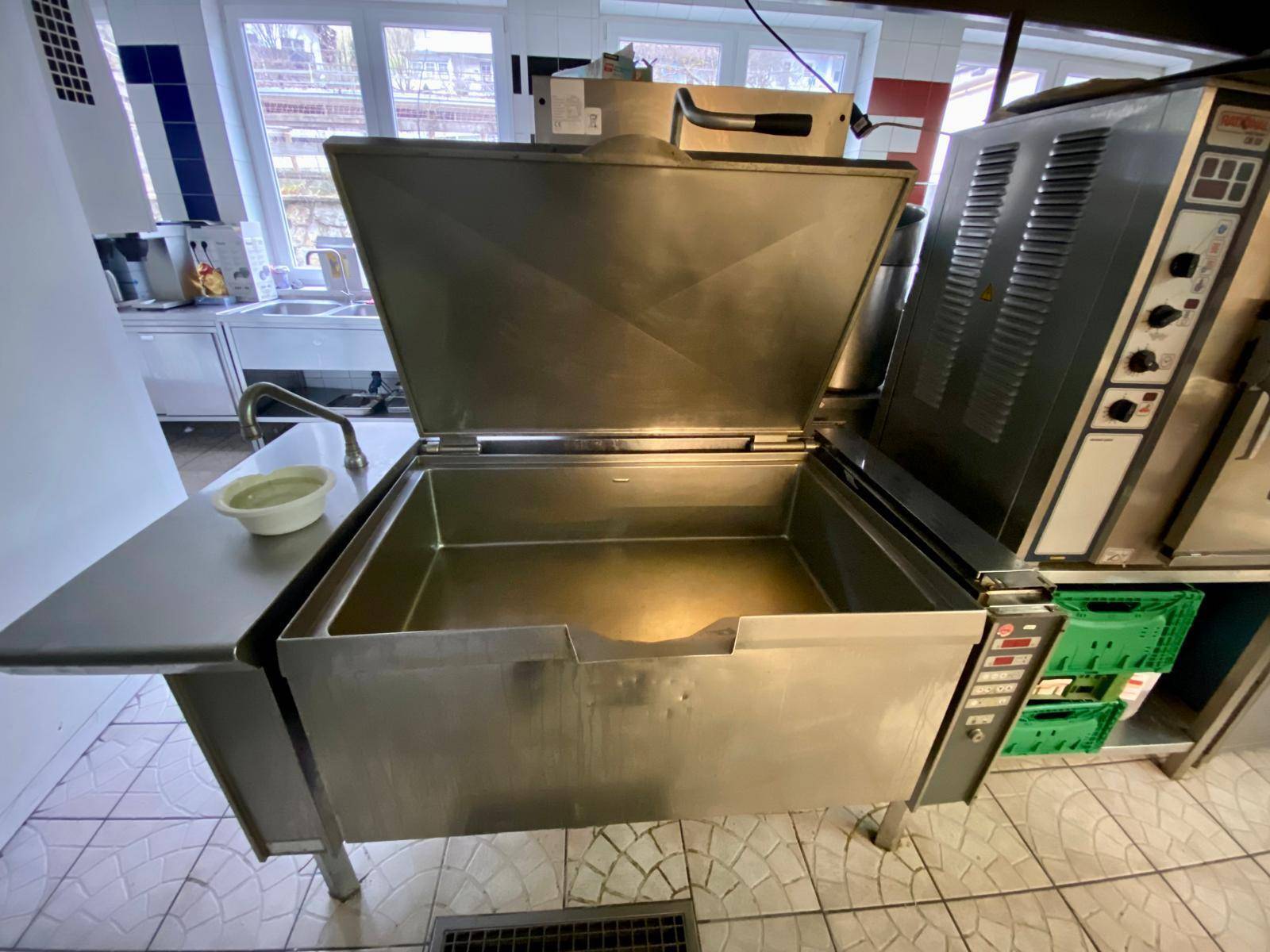 Nahaufnahme einer großen professionellen Kochwanne aus Edelstahl in einer Industrieküche.