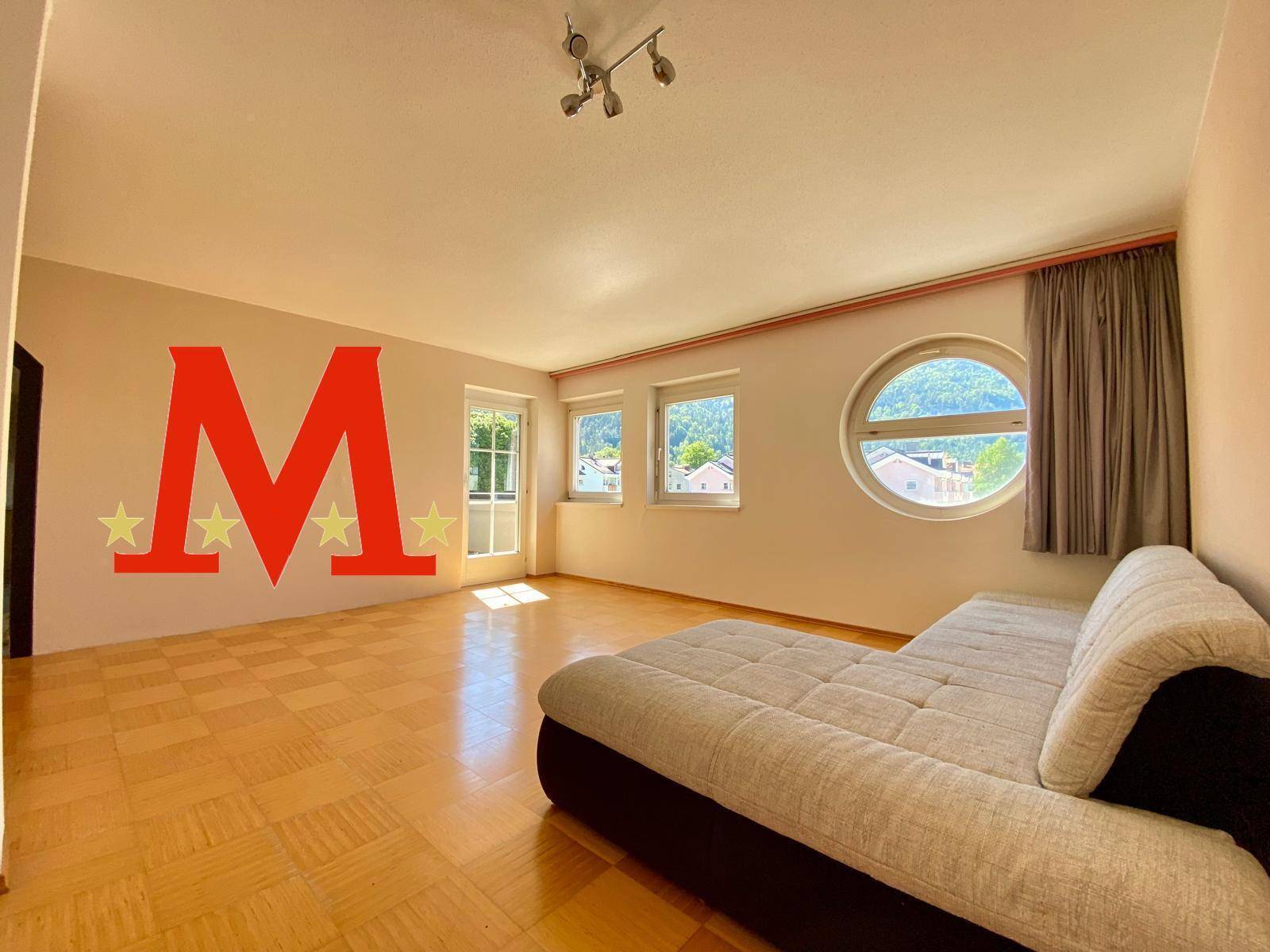 Helles Wohnzimmer mit Parkettboden, einem Sofa und verschiedenen Fenstern, darunter ein Rundfenster.