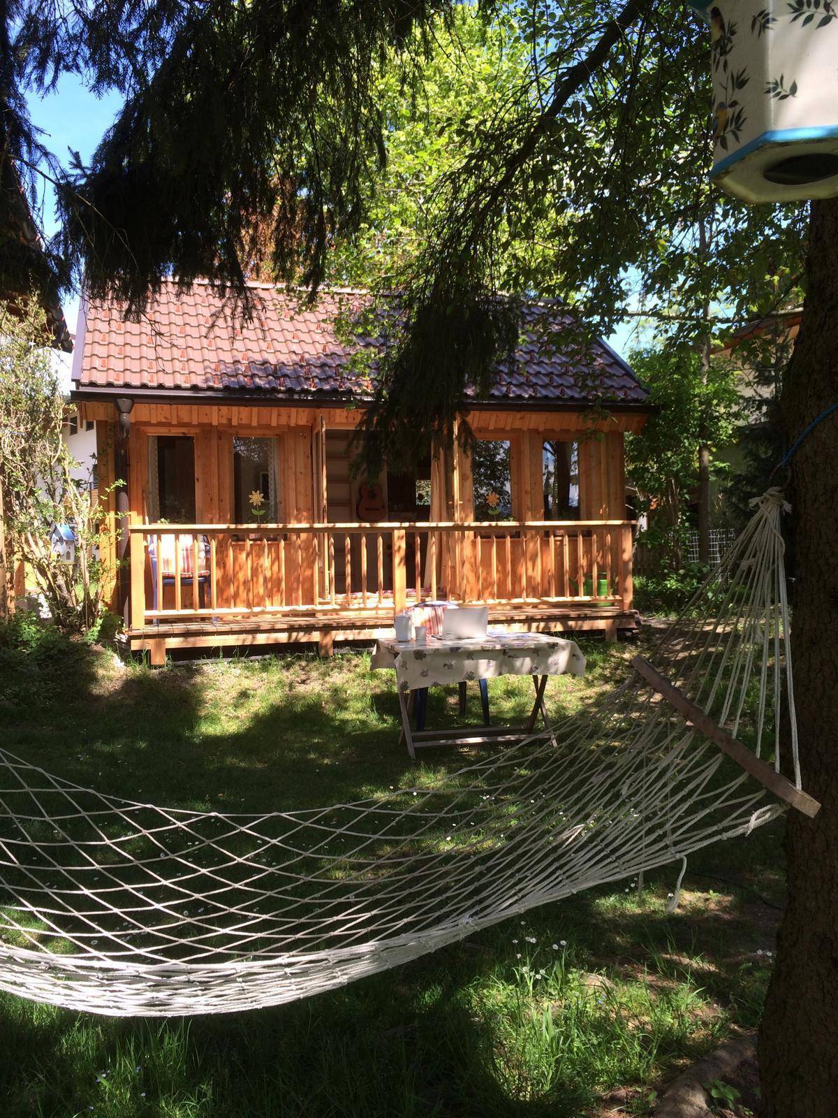 Gemütliche Holzhütte im Garten mit Hängematte und Sitzbereich im Freien.