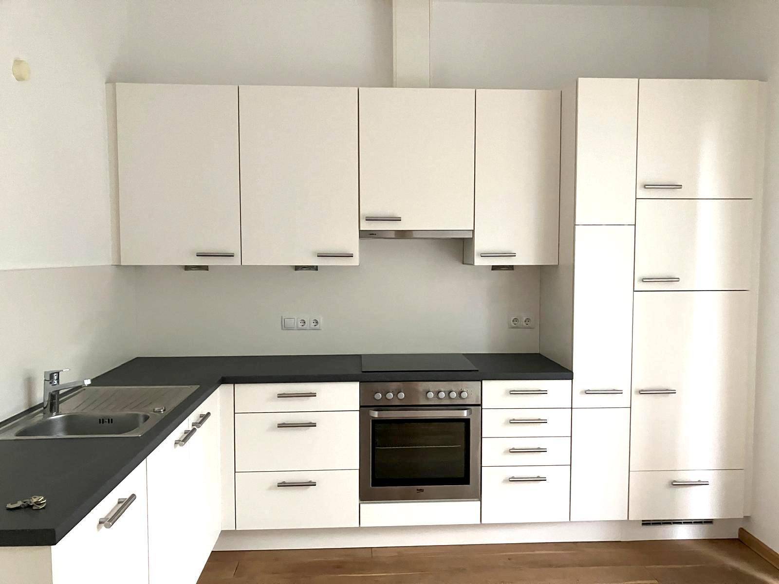 Neue Einbauküche mit weißen Schränken, dunkler Arbeitsplatte und integriertem Backofen.