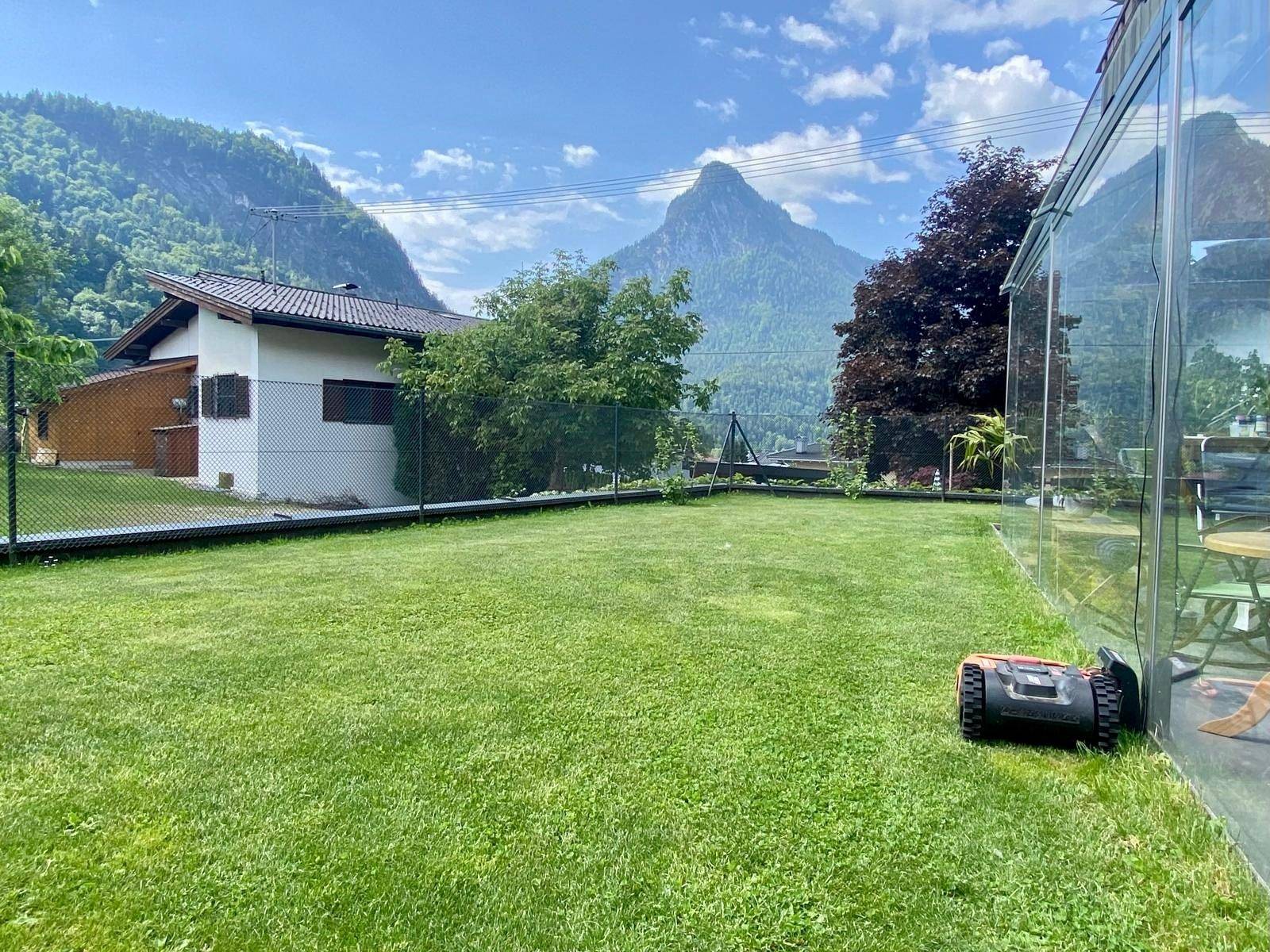 Großer, gepflegter Rasenbereich neben dem Wintergarten mit Bergblick im Hintergrund.