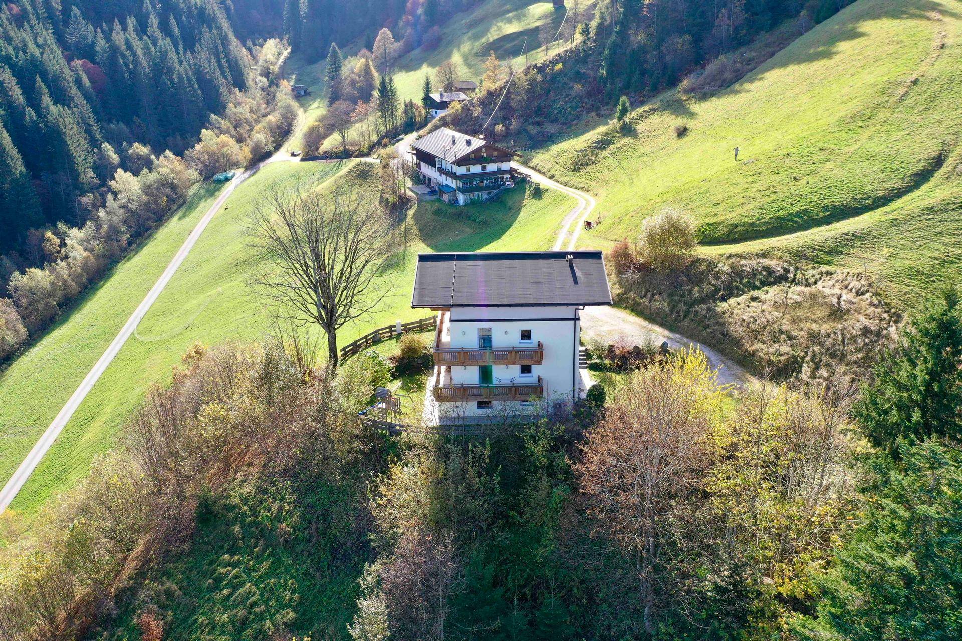 Luftaufnahme des Hauses in einer weitläufigen grünen Hügellandschaft mit Bergen im Hintergrund.
