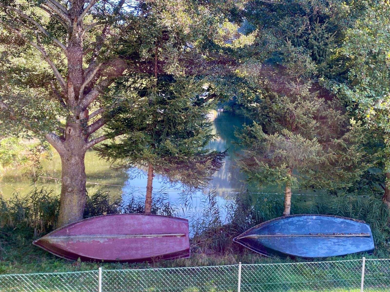 Ruhiger Seeabschnitt mit umgedrehten Booten am Ufer, umgeben von üppiger Vegetation und Bäumen.