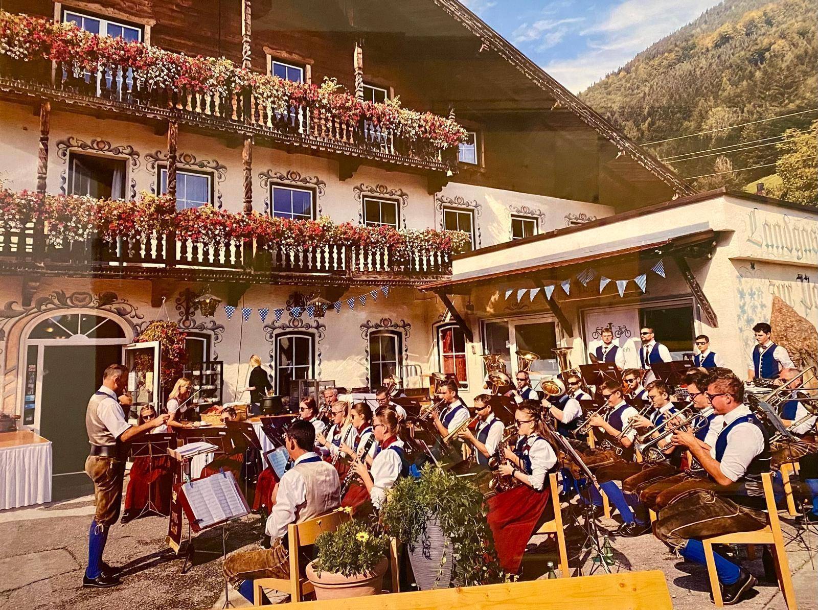 Traditionelles Gasthaus mit Musikkapelle und festlicher Dekoration im Außenbereich, umgeben von Bergen.