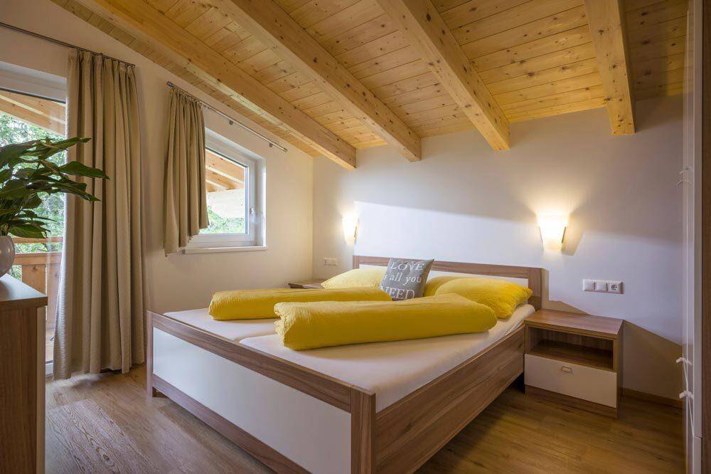 Helles Schlafzimmer mit Holzbalkendecke, Doppelbett und Zugang zum Balkon mit Bergblick.