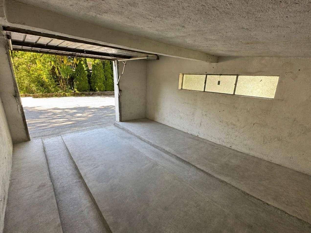 Innenansicht einer leeren Garage mit Betonboden und Blick nach draußen.