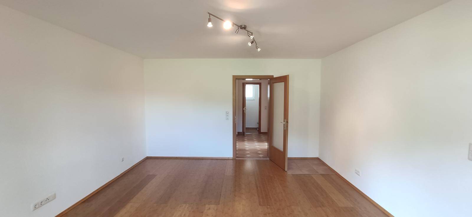 Geräumiges, leeres Zimmer mit hellem Holzparkett und weißen Wänden, bereit zur individuellen Gestaltung.