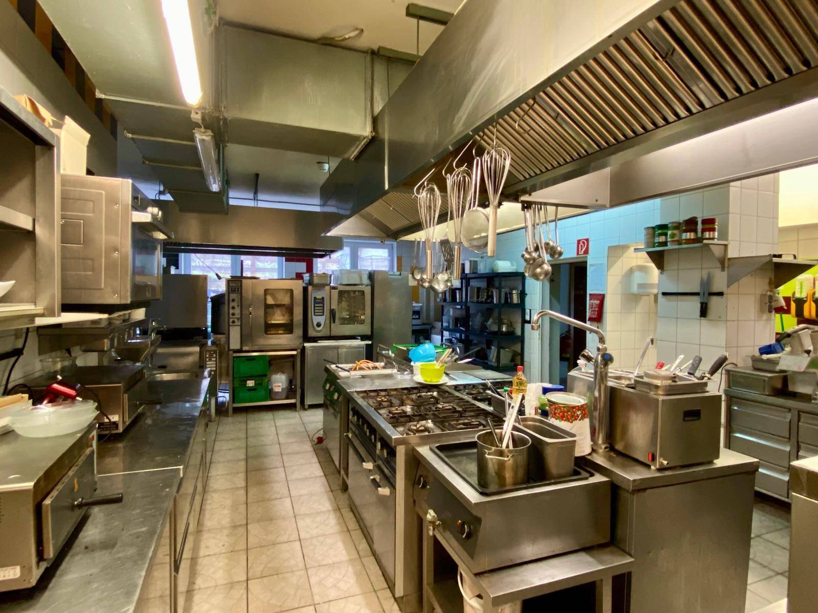 Große professionelle Küche mit Edelstahlgeräten, Gasherd und Ablufthaube für den Gastronomiebetrieb.