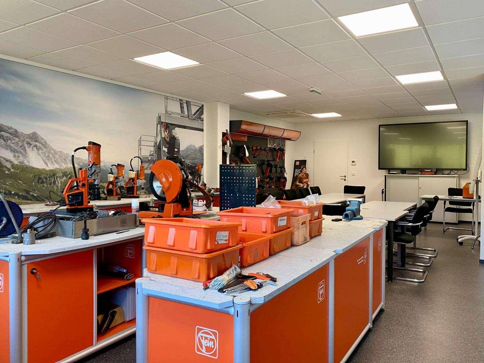 Werkstattbereich mit orangefarbenen Schränken, Arbeitsflächen und verschiedenen Werkzeugen, ausgestattet für praktische Arbeiten.