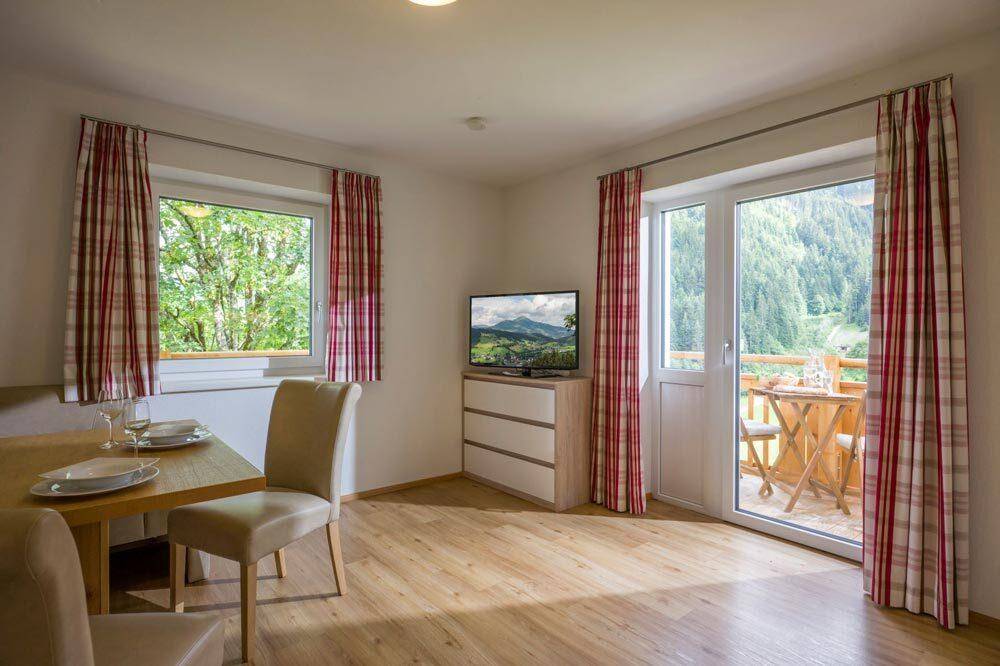 Heller Wohn- und Essbereich mit Holzboden, Fernseher und Zugang zu einem kleinen Balkon.